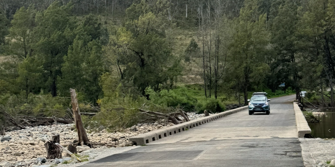 Blue car crossing river on road with trees in the background