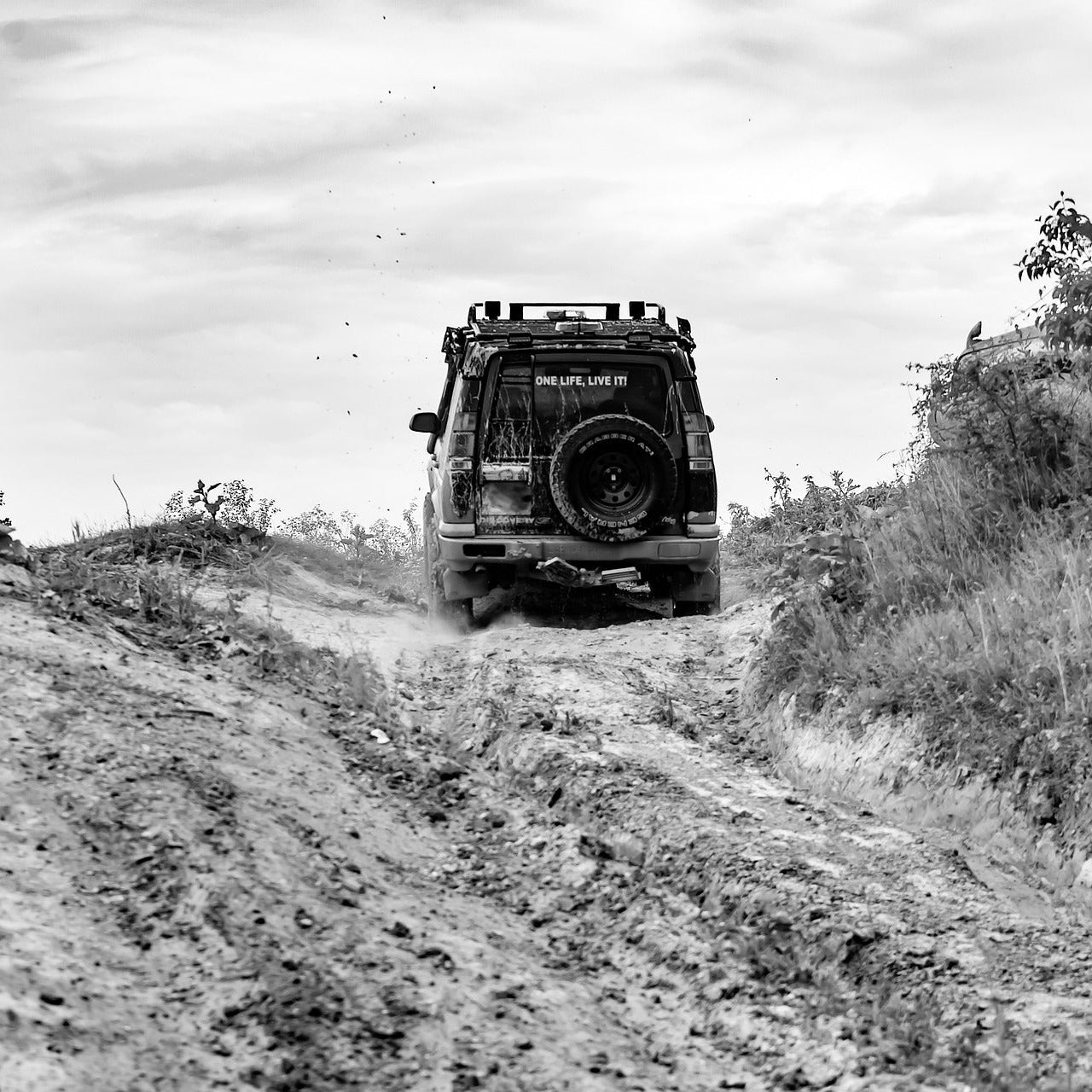 black and white image of four wheel drive driving up dirt track